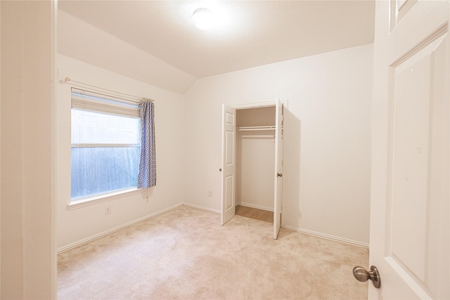 unfurnished bedroom with light carpet, lofted ceiling, and a closet