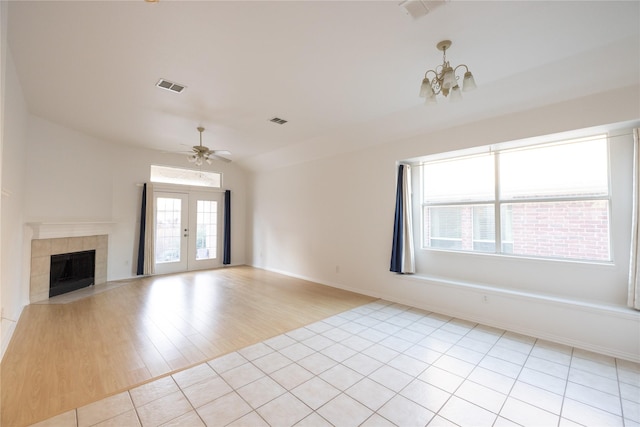 unfurnished living room featuring light tile patterned floors, a tiled fireplace, ceiling fan with notable chandelier, vaulted ceiling, and french doors