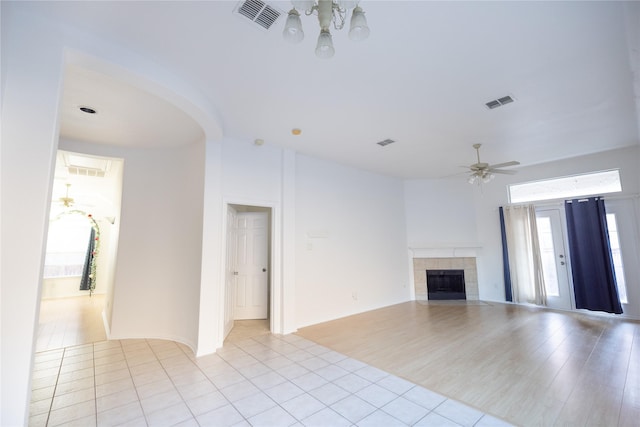 unfurnished living room featuring light tile patterned floors, ceiling fan with notable chandelier, and a fireplace