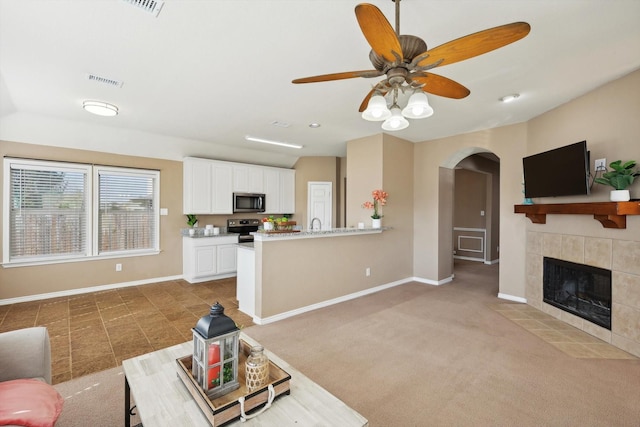 living area with visible vents, baseboards, light colored carpet, a tile fireplace, and arched walkways