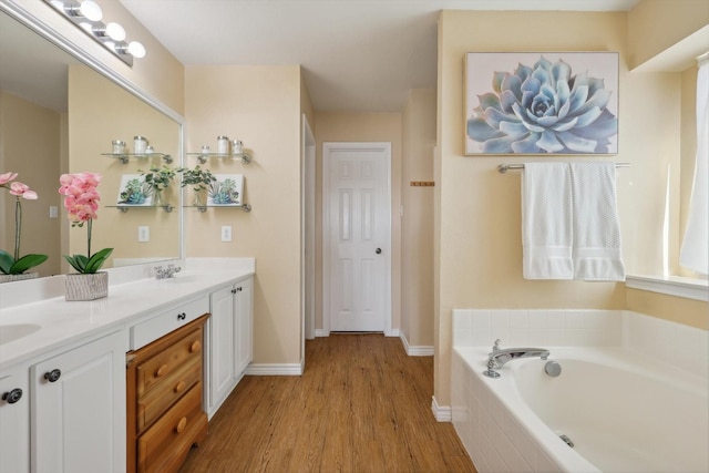 bathroom with wood finished floors, baseboards, double vanity, a sink, and a bath