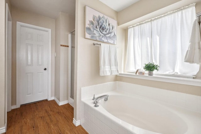 full bath featuring a stall shower, baseboards, a garden tub, and wood finished floors