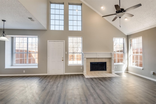 unfurnished living room with a tiled fireplace, wood-type flooring, a wealth of natural light, and a textured ceiling