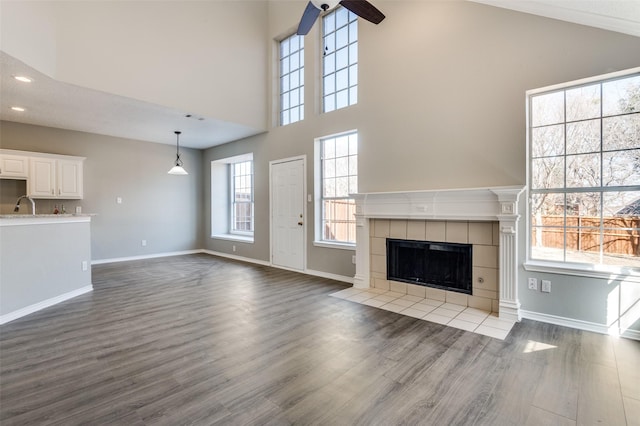 unfurnished living room with sink, a towering ceiling, a tile fireplace, and light wood-type flooring