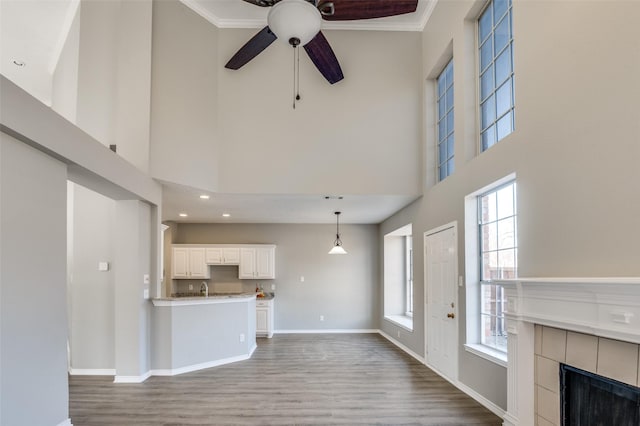 unfurnished living room with a tiled fireplace, a high ceiling, ceiling fan, crown molding, and light wood-type flooring