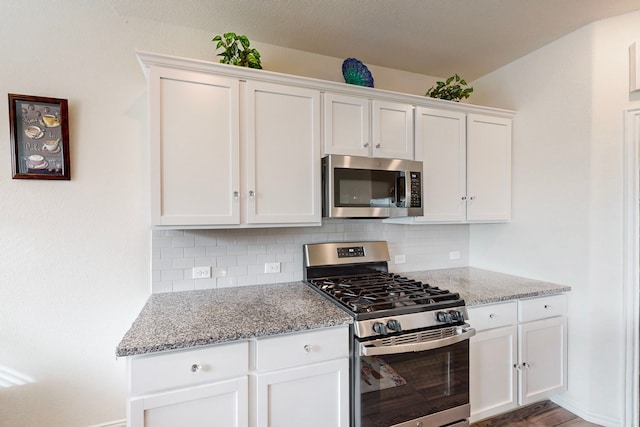 kitchen with white cabinets, decorative backsplash, hardwood / wood-style flooring, stainless steel appliances, and light stone countertops