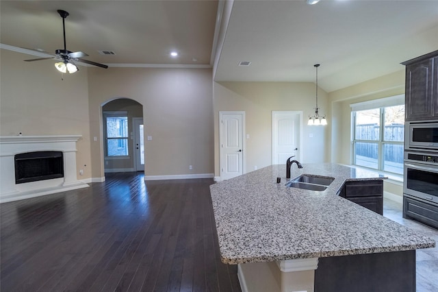 kitchen with dark brown cabinetry, sink, stainless steel appliances, light stone countertops, and a kitchen island with sink