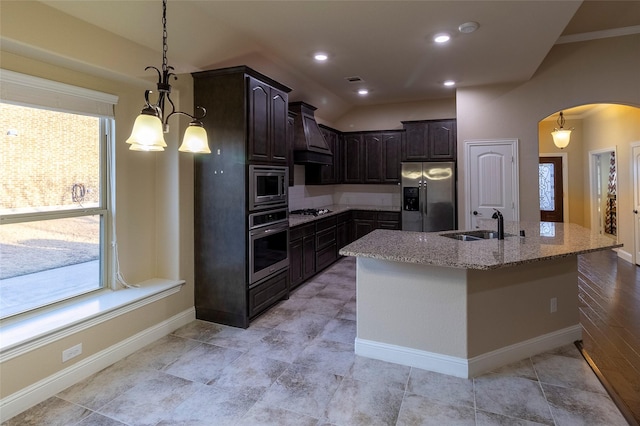 kitchen featuring light stone counters, hanging light fixtures, stainless steel appliances, and a center island with sink