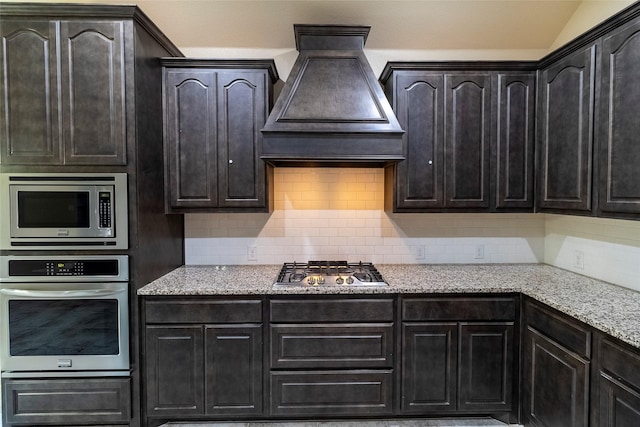 kitchen featuring custom exhaust hood, tasteful backsplash, light stone counters, vaulted ceiling, and stainless steel appliances