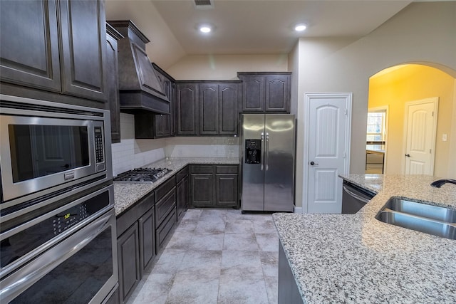 kitchen with dark brown cabinetry, sink, light stone counters, and appliances with stainless steel finishes