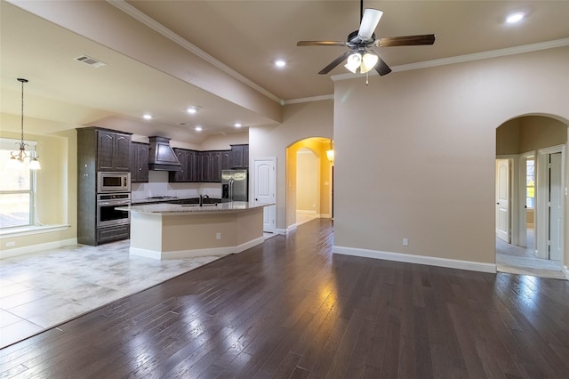 kitchen featuring appliances with stainless steel finishes, crown molding, dark brown cabinets, a center island with sink, and custom range hood