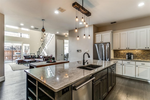 kitchen featuring appliances with stainless steel finishes, decorative light fixtures, white cabinetry, sink, and a kitchen island with sink