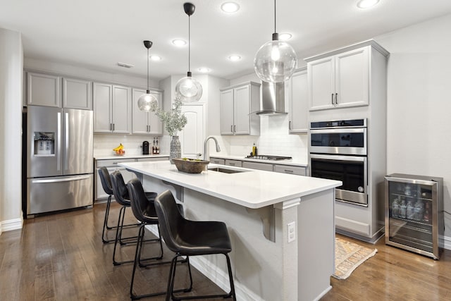 kitchen featuring pendant lighting, stainless steel appliances, beverage cooler, and wall chimney range hood