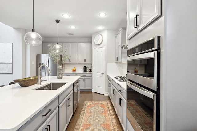 kitchen featuring sink, appliances with stainless steel finishes, tasteful backsplash, an island with sink, and decorative light fixtures