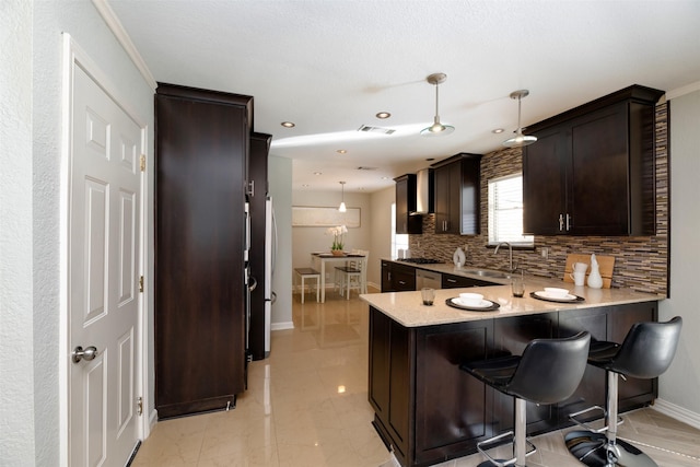 kitchen with tasteful backsplash, sink, hanging light fixtures, kitchen peninsula, and dark brown cabinets