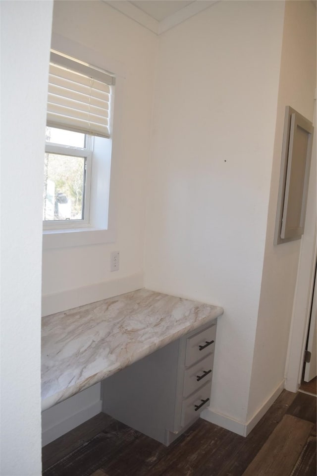 interior space with dark wood-type flooring, ornamental molding, and built in desk