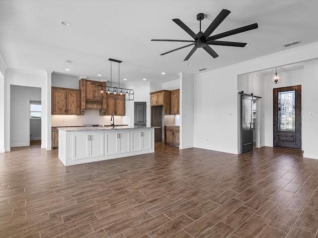 kitchen with decorative light fixtures, an island with sink, sink, ceiling fan, and a barn door