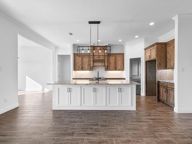 kitchen with sink, crown molding, light stone countertops, a center island with sink, and decorative light fixtures