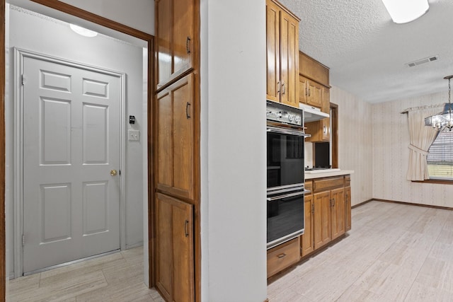 kitchen featuring pendant lighting, a textured ceiling, light hardwood / wood-style floors, and double oven