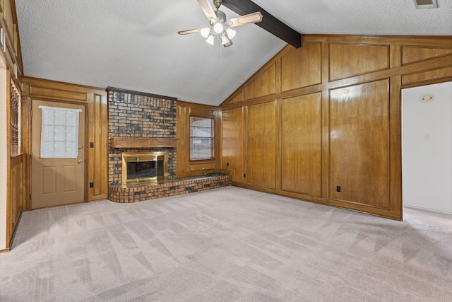 unfurnished living room featuring wood walls, lofted ceiling with beams, a textured ceiling, a brick fireplace, and light colored carpet