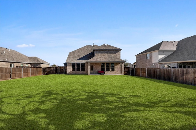 back of house with a fenced backyard, a lawn, and brick siding