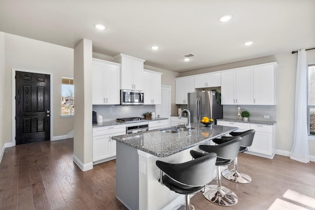 kitchen featuring decorative backsplash, dark wood-style floors, appliances with stainless steel finishes, a kitchen island with sink, and a sink