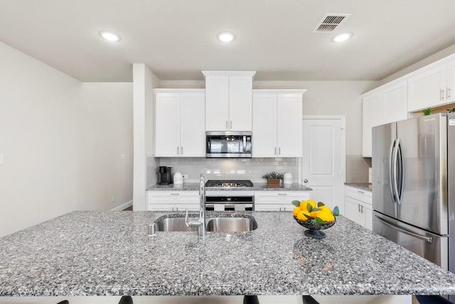 kitchen with tasteful backsplash, stone countertops, visible vents, appliances with stainless steel finishes, and a sink