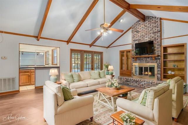 living room featuring french doors, vaulted ceiling with beams, light hardwood / wood-style flooring, a brick fireplace, and ceiling fan