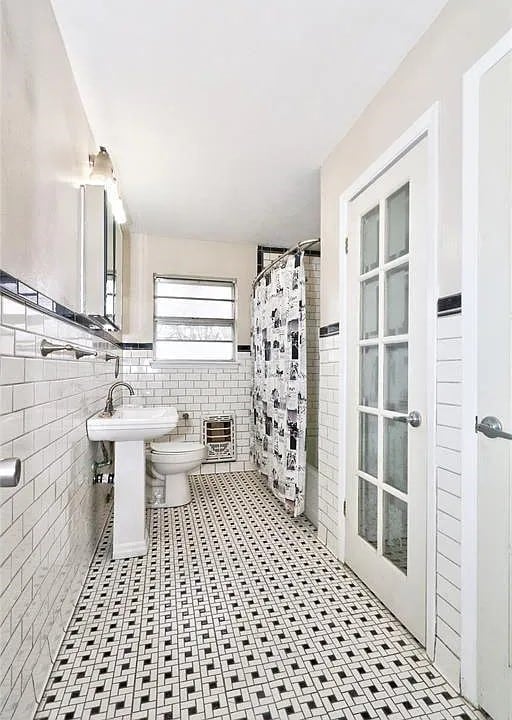 bathroom featuring toilet, curtained shower, sink, and tile walls