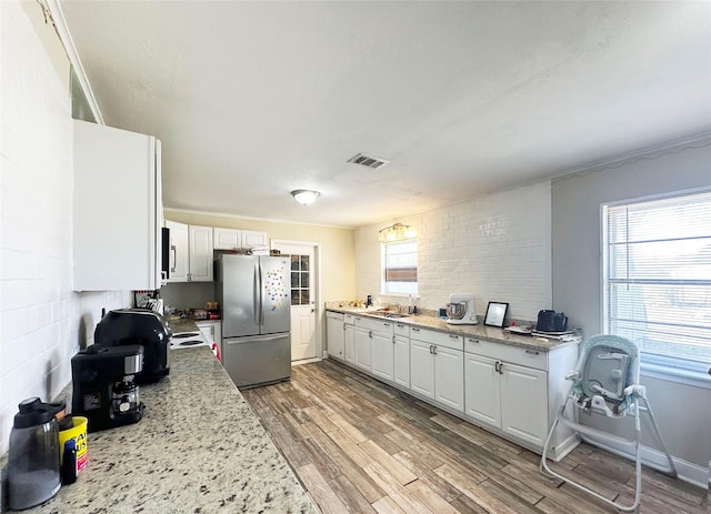 kitchen featuring light stone countertops, appliances with stainless steel finishes, white cabinets, and light hardwood / wood-style floors