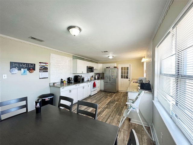 kitchen with white cabinetry, appliances with stainless steel finishes, ornamental molding, and light stone counters