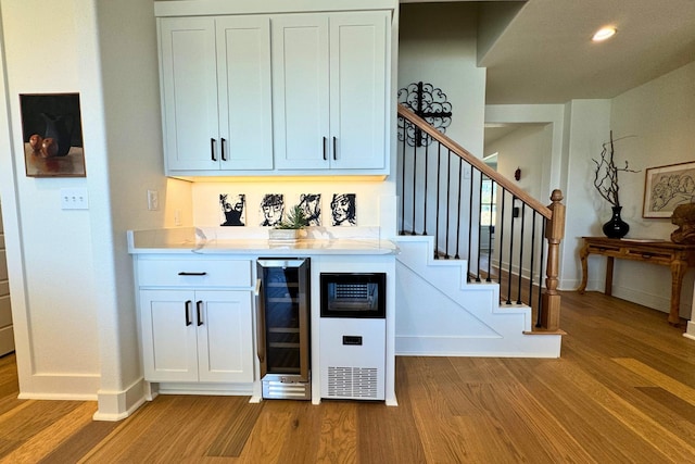 bar with stairs, beverage cooler, baseboards, and wood finished floors