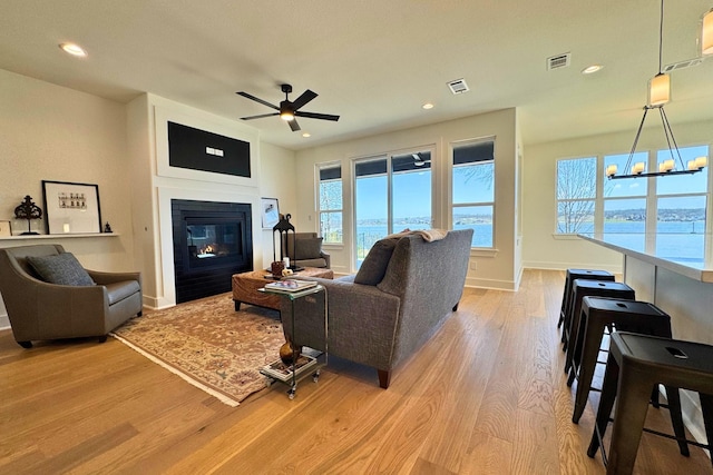 living room with light wood-style floors, recessed lighting, visible vents, and a glass covered fireplace