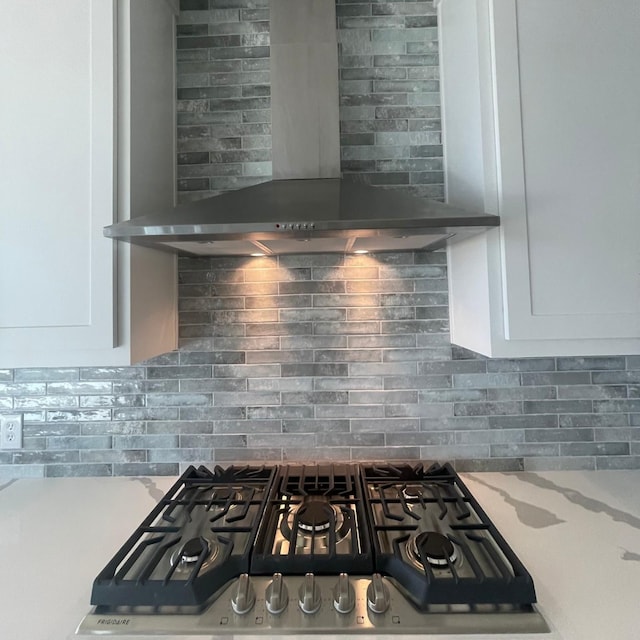 room details featuring backsplash, white cabinets, stainless steel gas cooktop, and wall chimney range hood