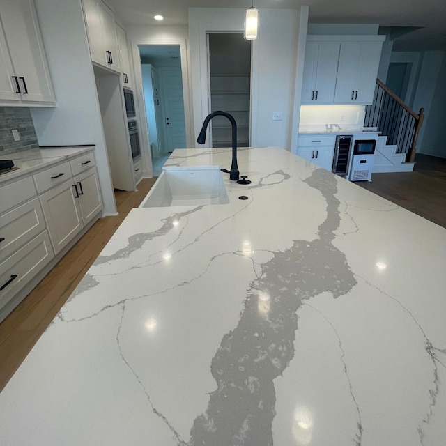 kitchen featuring hanging light fixtures, light stone countertops, sink, and white cabinets