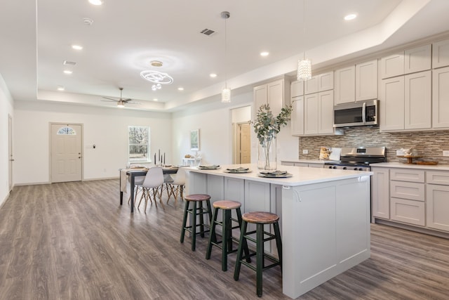 kitchen featuring a kitchen island, decorative light fixtures, a raised ceiling, a kitchen breakfast bar, and stainless steel appliances