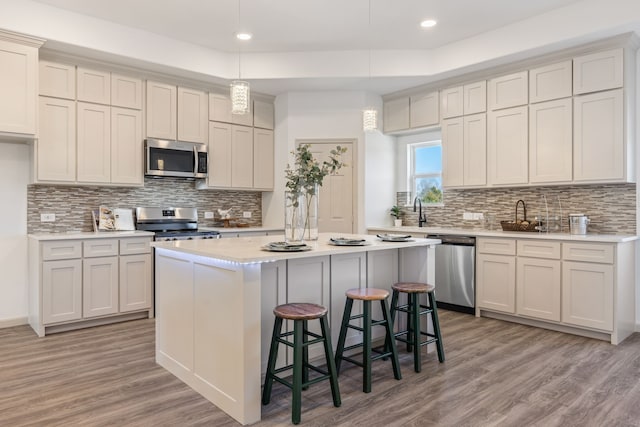 kitchen with a kitchen bar, appliances with stainless steel finishes, a kitchen island, pendant lighting, and light hardwood / wood-style floors