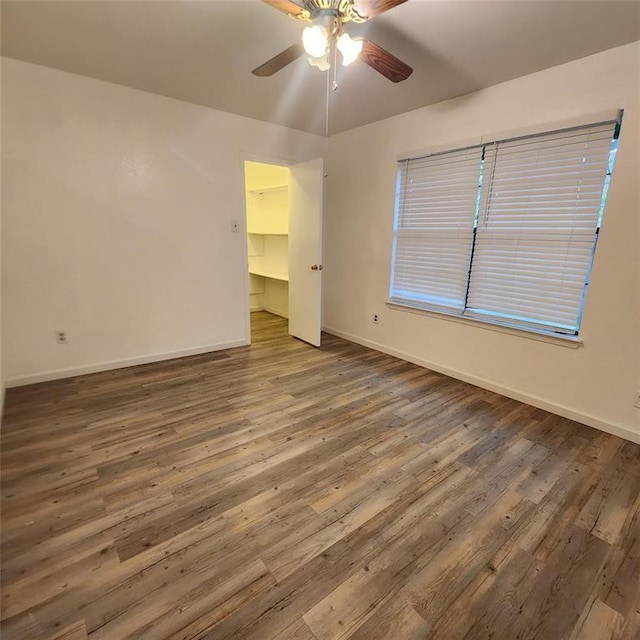 unfurnished bedroom featuring a walk in closet, dark hardwood / wood-style floors, ceiling fan, and a closet