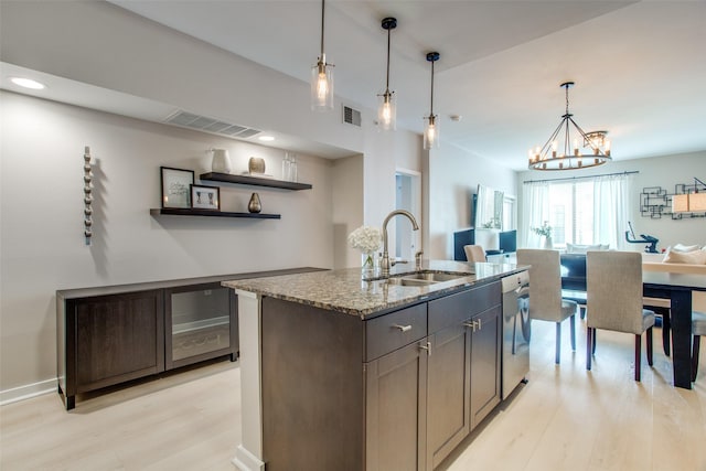 kitchen featuring sink, dark brown cabinets, light stone countertops, an island with sink, and light wood-type flooring