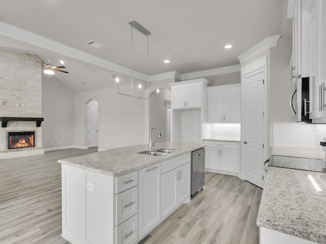 kitchen with white cabinetry, hanging light fixtures, stainless steel appliances, light stone countertops, and a center island with sink