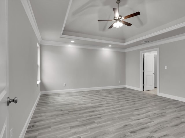 empty room with crown molding, light wood-type flooring, ceiling fan, and a tray ceiling