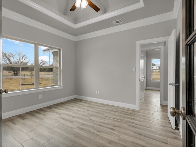 empty room with a raised ceiling, crown molding, ceiling fan, and light hardwood / wood-style flooring