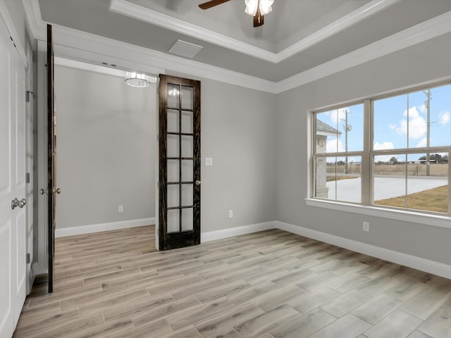 spare room featuring a raised ceiling, crown molding, ceiling fan, and light wood-type flooring