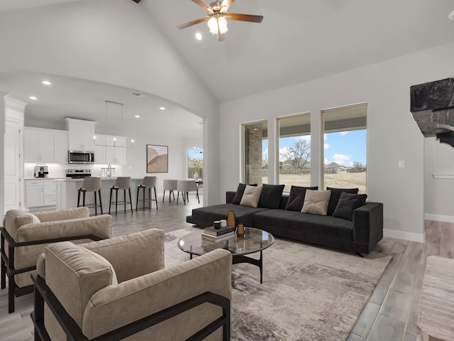 living room with ceiling fan, plenty of natural light, high vaulted ceiling, and light hardwood / wood-style floors