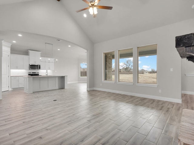 unfurnished living room with ceiling fan, sink, beam ceiling, and high vaulted ceiling