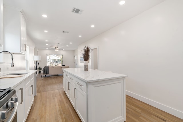 kitchen with stainless steel range oven, sink, light stone counters, a center island, and white cabinets