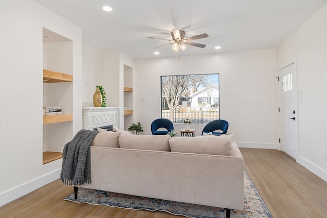 living room featuring built in shelves, light hardwood / wood-style floors, and ceiling fan