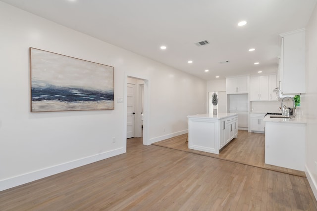 kitchen with light wood-type flooring, sink, a kitchen island, and white cabinets