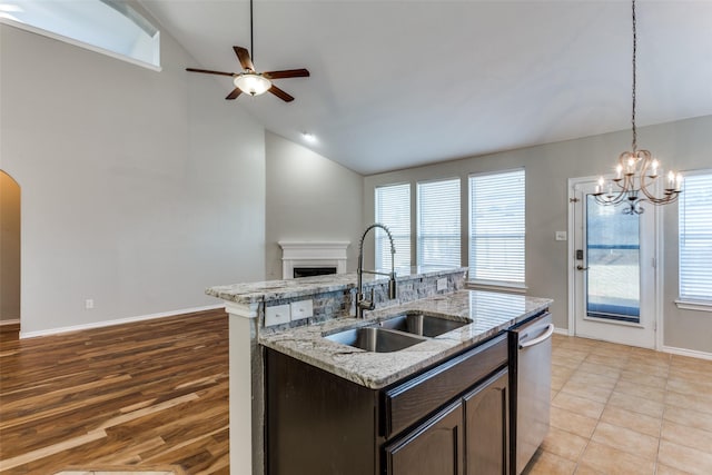 kitchen featuring sink, light stone counters, dark brown cabinets, dishwasher, and a kitchen island with sink