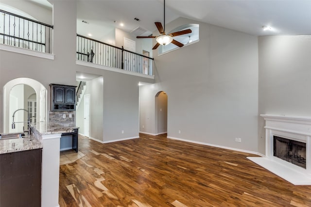 unfurnished living room with dark hardwood / wood-style flooring, sink, ceiling fan, and a high ceiling